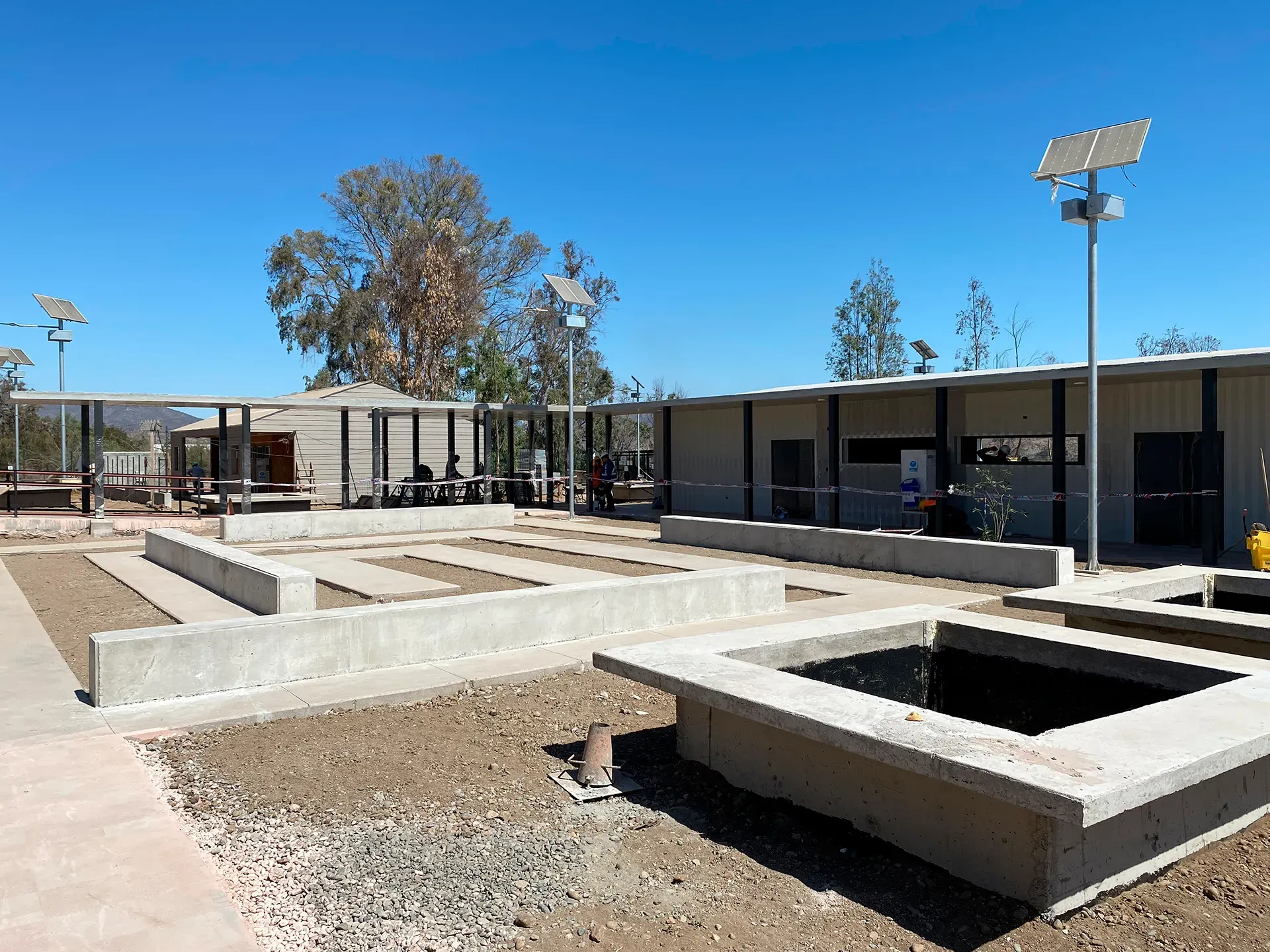Escuela San Antonio de la Villa Barraza: pabellones con techumbre de acero y luminarias solares, con las obras exteriores aún en ejecución en primer plano.